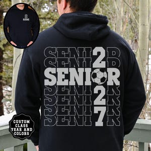 May include: A black hooded sweatshirt featuring a large back graphic with the word SENIOR repeated in white outline text, the number 2027 in large white font, and a soccer ball graphic. The front chest area displays the word NAME in white text.
