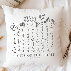 May include: White cushion with a grey floral design and the text "FRUITS OF THE SPIRIT GALATIANS 5:22".