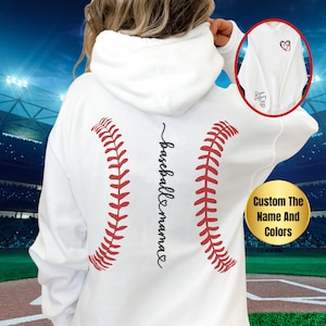 May include: White hoodie with a baseball graphic and the text "baseball mama" on the back. The hoodie is shown on a model in front of a baseball stadium.