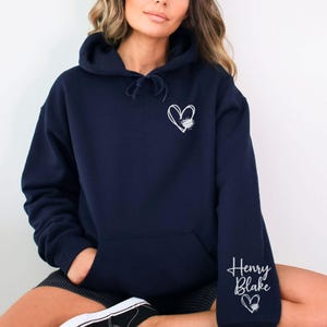K&ouml;nnte beinhalten: Dunkelblauer Hoodie mit einem wei&szlig;en Herzdesign auf der Vorderseite und dem Namen "Henry Blake" sowie einem wei&szlig;en Herzdesign auf dem linken &Auml;rmel.