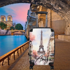 May include: A black suitcase with a watercolor design of the Eiffel Tower in Paris, France. The suitcase has the name "Arya" written on it.