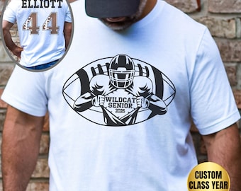 May include: A white t-shirt featuring a black graphic of a football player tearing open their jersey to reveal the text WILDCAT SENIOR 2026. An inset shows the back of the shirt with the name ELLIOTT and the number 44 in brown and white.