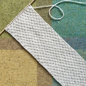 Könnte beinhalten: Nahaufnahme eines weißen gestrickten Stoffes mit einem strukturierten Muster. Der Stoff liegt auf einer mehrfarbigen Oberfläche.