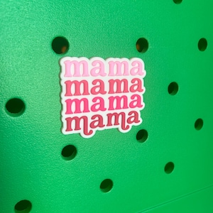 May include: A white sticker with the word "mama" repeated four times in pink and red lettering. The sticker is on a green surface.