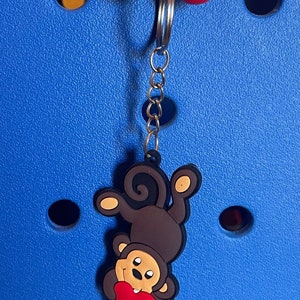 May include: A brown monkey charm with a red heart, hanging from a silver keychain with red and white beads.