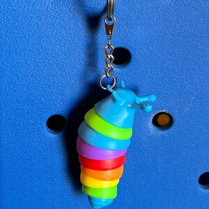 May include: A colorful rainbow slug charm with a silver key chain and a blue and white bead charm with the letter "b" on it.