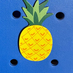 May include: A yellow pineapple with a green leafy top on a blue background. The pineapple has a textured pattern of orange lines.