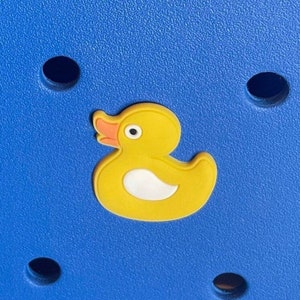 K&ouml;nnte beinhalten: Ein gelber Gummiente-Anh&auml;nger mit wei&szlig;em Bauch und orangefarbenem Schnabel auf blauem Hintergrund.