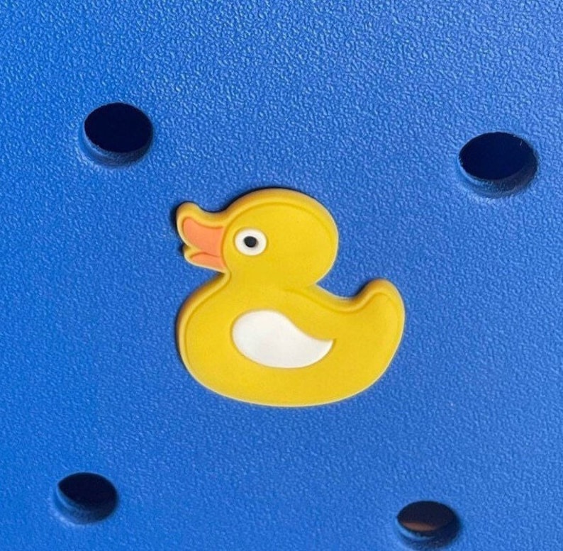 K&ouml;nnte beinhalten: Ein gelber Gummiente-Anh&auml;nger mit wei&szlig;em Bauch und orangefarbenem Schnabel auf blauem Hintergrund.