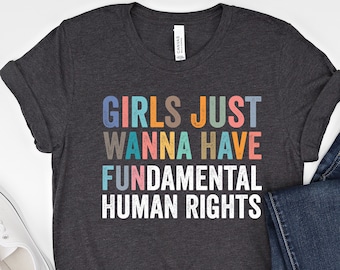 May include: A dark heather grey t-shirt with the text "Girls Just Wanna Have Fundamental Human Rights" printed in rainbow colors.