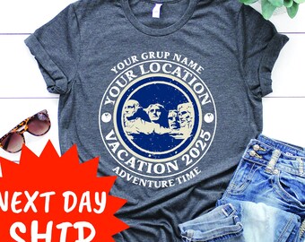 May include: Dark gray t-shirt with a circular graphic featuring Mount Rushmore and the text "Your Group Name, Your Location, Vacation 2025, Adventure Time." The shirt is paired with blue denim shorts and sunglasses.