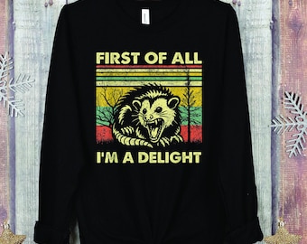 May include: Black long-sleeved shirt with a retro-style graphic of a possum with the text "First of all I'm a delight".
