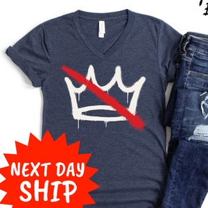 May include: Navy blue V-neck t-shirt with a white crown graphic crossed out with a red line. The image also shows a pair of blue jeans with distressed details. The text "CyberART Blocks" is in the upper right corner.