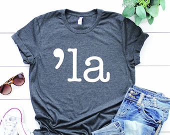May include: A dark gray t-shirt with a white graphic of an apostrophe and the word "'la" printed on the front.