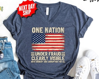 May include: A heather navy blue V-neck t-shirt featuring a distressed American flag graphic. The text reads ONE NATION UNDER FRAUD CLEARLY VISIBLE WITH BRIBERY AND CORRUPTION FOR ALL. The shirt is displayed alongside blue jeans and white sneakers.