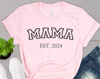 May include: Pink t-shirt with black text that reads "MAMA EST. 2024".