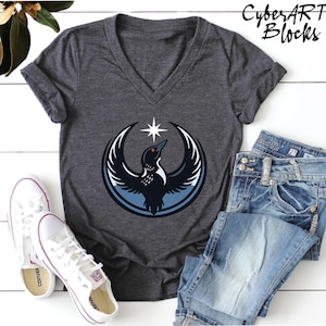 a gray v-neck t-shirt with a graphic design, a pair of white sneakers, and a pair of blue jeans laid out on a white surface.