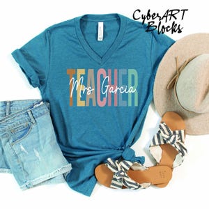 a t - shirt that says teacher next to a pair of jeans and a hat