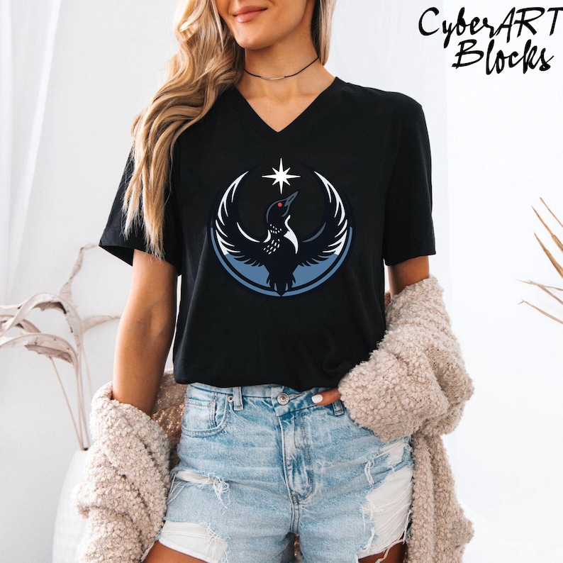 A woman wearing a black t-shirt with a graphic design of a bird and a star, paired with distressed denim shorts and a beige cardigan.