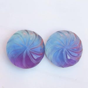 May include: Two round, iridescent glass cabochons with a swirling, flower-like design. The cabochons are a gradient of blue, purple, and pink.