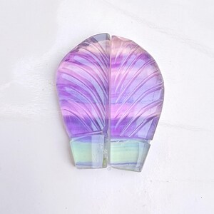 Könnte beinhalten: Zwei geschnitzte Fluoritstein-Hälften, jede mit einem Farbverlauf von Lila, Rosa und Grün. Die Hälften werden zu einer Blattform zusammengefügt.