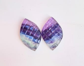 Puede incluir: Dos cabujones de fluorita iridiscente de color púrpura, azul y verde con un patrón geométrico. Los cabujones tienen forma de hoja y un acabado liso y pulido.