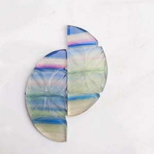 Könnte beinhalten: Zwei Halbkreisstücke aus geschnitztem Fluorit, jedes mit einem anderen Farbmuster. Das obere Stück ist hellblau, grün und rosa, während das untere Stück dunkelblau, grün und rosa ist. Beide Stücke haben ein geschnitztes Blumendesign.