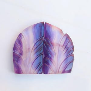 Könnte beinhalten: Zwei geschnitzte Achat-Cabochons in Lila und Weiß mit einem Blattdesign. Die Cabochons sind poliert und haben eine glatte, glänzende Oberfläche.