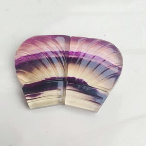 Könnte beinhalten: Zwei geschnitzte Fluorit-Cabochons, einer lila und weiß, der andere gelb und weiß, mit einem fächerförmigen Muster.