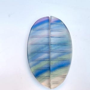 Könnte beinhalten: Ein glasartiges Blatt-förmiges Ornament mit einem abstrakten Design in Blau, Grün und Rosa. Das Ornament ist in zwei Hälften geteilt und die beiden Hälften sind miteinander verbunden.