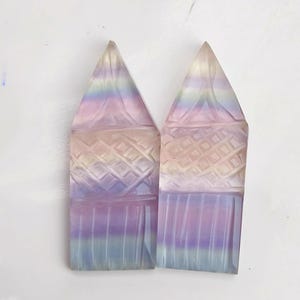 Könnte beinhalten: Zwei regenbogenfarbene, geschnitzte Fluorit-Kristallspitzen in Lila, Blau und Gelb. Die Spitzen sind mit einem geometrischen Muster geschnitzt und haben eine glatte, polierte Oberfläche.