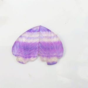 Könnte beinhalten: Zwei geschnitzte Fluoritsteine ​​in Herzform in den Farben Lila und Weiß.