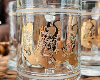 May include: Clear glass tumblers with gold and white accents. Each tumbler features a gold cowboy boot design. The glasses have a white band near the top and bottom. The image shows a close-up of the glasses.