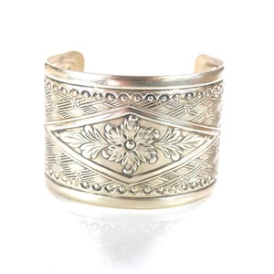 Puede incluir: Pulsera de brazalete de plata con un intrincado diseño floral y un patrón geométrico.