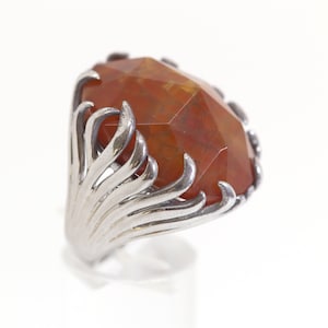 May include: A silver ring with a large, faceted, orange gemstone set in a stylized, fan-shaped design.