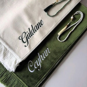 Puede incluir: Una alfombra de oración color crema con el nombre bordado Güldane y una alfombra de oración verde con el nombre bordado Ceyhun. Ambas alfombras tienen bordes con flecos y vienen con dos rosarios, uno verde y otro blanco con borlas.