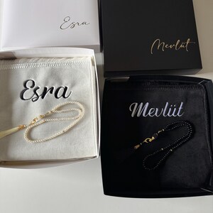 May include: Two gift boxes containing prayer beads. The white box features the name Esra and contains a white velvet pouch with the name Esra and white pearl beads. The black box features the name Mevl&uuml;t and a black pouch with black beads.