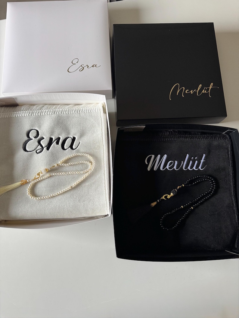 May include: Two gift boxes containing prayer beads. The white box features the name Esra and contains a white velvet pouch with the name Esra and white pearl beads. The black box features the name Mevl&uuml;t and a black pouch with black beads.