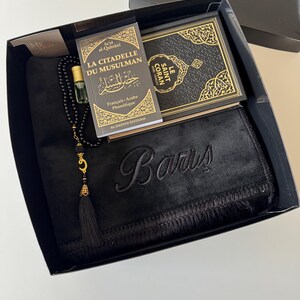 K&ouml;nnte beinhalten: Eine schwarze Geschenkbox mit einem schwarzen Gebetsteppich, auf dem der Name Baris schwarz eingestickt ist, einer schwarz-goldenen Gebetskette, einem kleinen Glasflakon f&uuml;r Parf&uuml;m sowie den B&uuml;chern La Citadelle du Musulman und Le Saint Coran.