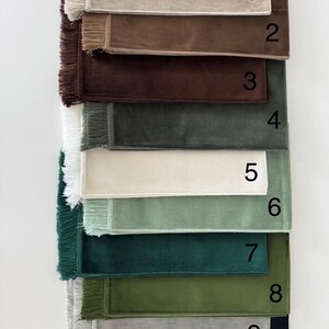 K&ouml;nnte beinhalten: Eine Sammlung von zehn rechteckigen Stoffmustern mit Fransen an der linken Seite, vertikal angeordnet. Jedes Muster hat eine einzigartige einfarbige Farbe, darunter Beige, Braun, Dunkelbraun, Grau, Wei&szlig;, Hellgr&uuml;n, T&uuml;rkis, Oliv, Silber und Schwarz.