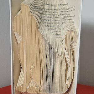 Op de afbeelding: Een boeksculptuur met gevouwen pagina's om een driedimensionaal ontwerp te creëren. De pagina's zijn beige en het boek is open, waardoor de ingewikkelde vouwen en uitgesneden vormen zichtbaar zijn. Het boek staat op een rode ondergrond.