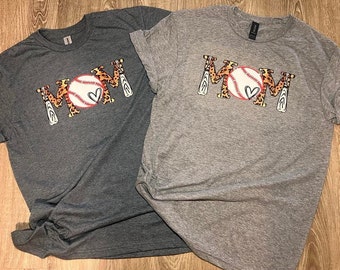 Könnte beinhalten: Zwei graue T-Shirts mit dem Wort "MOM" in Leopardenmuster mit einem Baseball und Schlägern.
