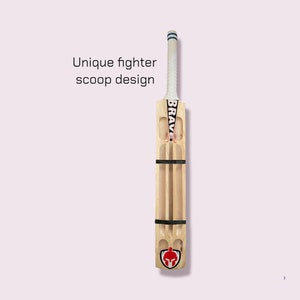 May include: A wooden cricket bat with a unique scoop design. The bat is brown with black tape and a white grip. The bat has the word "BRAVE" printed on it in black letters. The bat has a red and black logo of a warrior's helmet on the bottom.