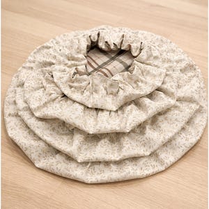 May include: A set of three nested circular fabric bowl covers featuring a light beige background with a small repeating leaf pattern. The covers have elasticized edges for a snug fit, and the innermost cover reveals a brown and white plaid lining.