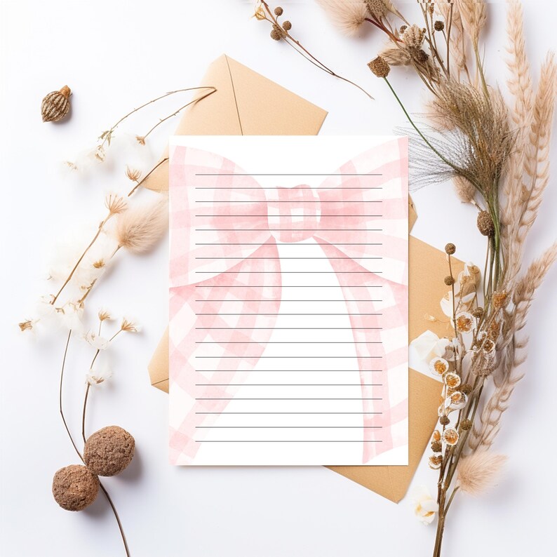Peut inclure: Une feuille de papier &agrave; lettres lign&eacute;e avec un motif de n&oelig;ud rose. Le n&oelig;ud a un motif vichy et se trouve en haut au centre de la page. La papeterie est sur une surface blanche avec des fleurs s&eacute;ch&eacute;es et une enveloppe marron.