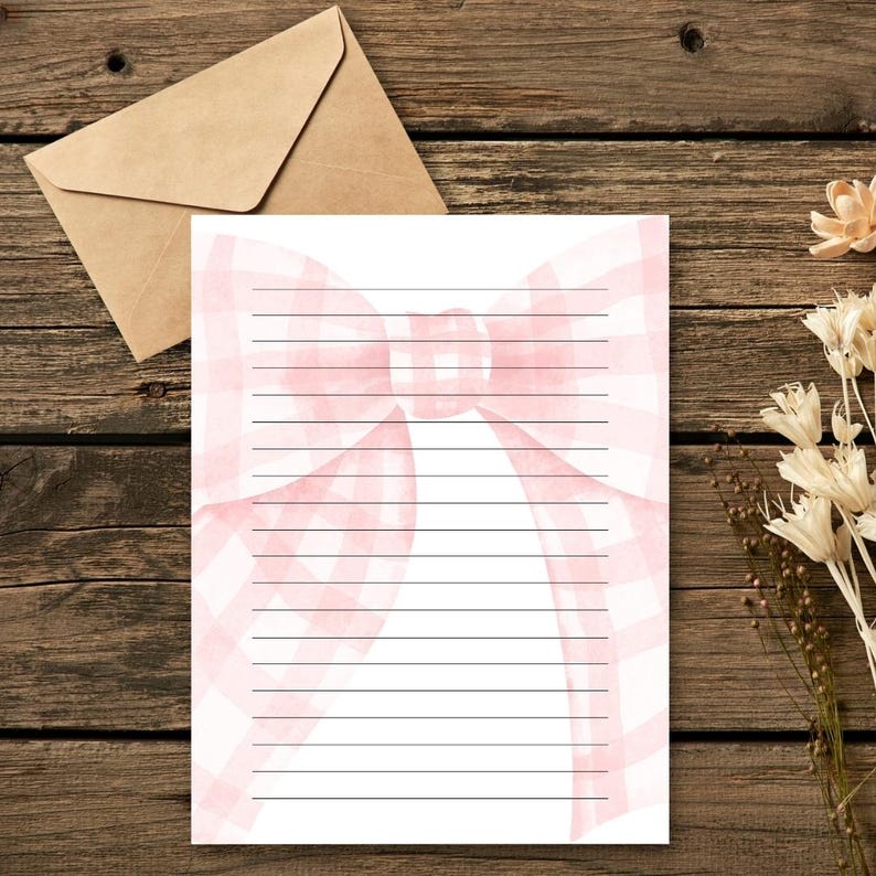 Peut inclure: Papier &agrave; lettres lign&eacute; avec un motif de n&oelig;ud rose &agrave; carreaux. Une enveloppe marron est en arri&egrave;re-plan, ainsi que des fleurs s&eacute;ch&eacute;es, le tout sur une surface en bois. Parfait pour &eacute;crire des lettres.