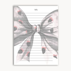 Peut inclure: Un bloc-notes lign&eacute; avec un motif de n&oelig;ud papillon &agrave; l'aquarelle. Le n&oelig;ud est gris avec des accents noirs et roses. Le mot "Notes" est &eacute;crit en cursive en haut de la page.