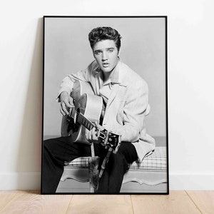 May include: Black and white photo of Elvis Presley sitting and playing an acoustic guitar.