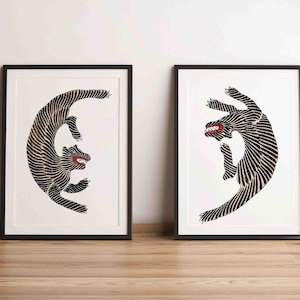 Puede incluir: Dos impresiones artísticas enmarcadas con ilustraciones estilizadas de tigres en blanco y negro con bocas rojas. Los tigres se representan en una pose curva dinámica sobre un fondo blanco. Los marcos son negros.
