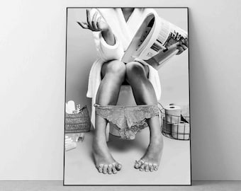 May include: Black and white photo of a person sitting on a toilet, wearing a white robe and reading a magazine. The person is wearing underwear with a lace design.